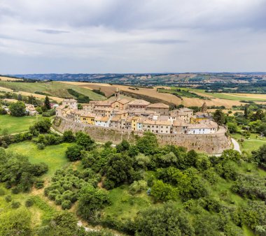 An aerial view north east toward the hilltop fortress village of Sant Andrea di Suasa, Italy in summertime clipart