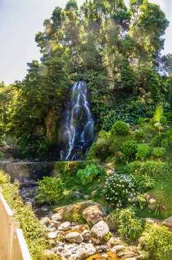 A long exposure view up a path towards a walled waterfall at the Ribeiria waterfalls on the island of Sao Miguel in the Azores in summertime clipart