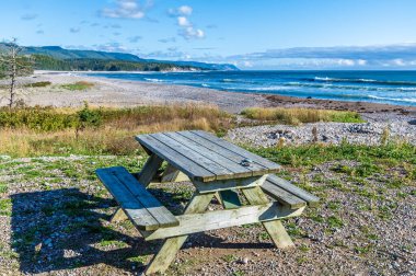 A view past a picnic bench over the beach at Little River Harbour on the Cabot Trail, Nova Scotia, Canada in the fall clipart