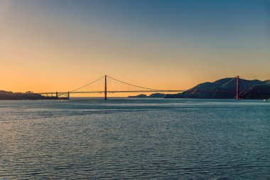 Baharın erken saatlerinde San Francisco 'daki körfezden gün batımına doğru Golden Gate Köprüsü' ne doğru bir manzara.