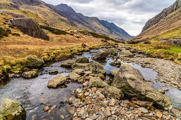 İlkbaharda Galler, Snowdonia 'daki Idwal Gölü' nden akan bir köprünün manzarası.