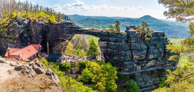 İlkbaharda ağaçların arasından Pravcicka Kapısı kemerine doğru bir manzara