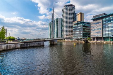 Manchester kanalı boyunca yazları Media City, Manchester, İngiltere 'ye giden bir yaya köprüsüne bakan bir manzara