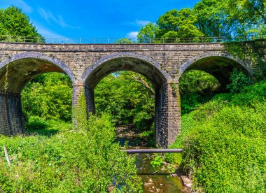 Yazın New Mills 'de bulunan Goyt Nehri' nin karşısındaki bir köprüye doğru uzanan bir manzara, İngiltere 'de Yüksek Tepe.