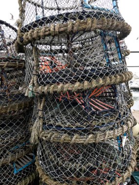 Karışık balık ağlarının ve ıstakoz tuzaklarının detaylı görüntüsü, kıyı balıkçılık endüstrisinde kullanılan deniz ekipmanları. Sürdürülebilir deniz ürünleri koleksiyonu için hayati önem taşıyan rustik dokuları ve zanaatkarlığı gösterir.