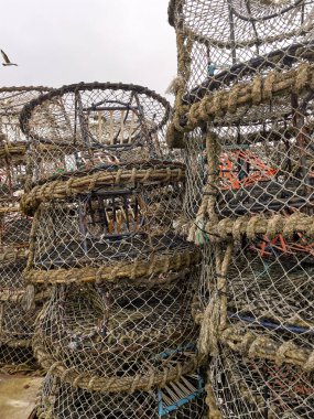 Karışık balık ağlarının ve ıstakoz tuzaklarının detaylı görüntüsü, kıyı balıkçılık endüstrisinde kullanılan deniz ekipmanları. Sürdürülebilir deniz ürünleri koleksiyonu için hayati önem taşıyan rustik dokuları ve zanaatkarlığı gösterir.