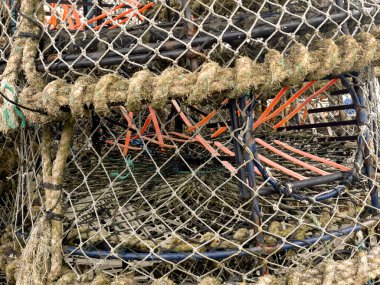 Karışık balık ağlarının ve ıstakoz tuzaklarının detaylı görüntüsü, kıyı balıkçılık endüstrisinde kullanılan deniz ekipmanları. Sürdürülebilir deniz ürünleri koleksiyonu için hayati önem taşıyan rustik dokuları ve zanaatkarlığı gösterir.