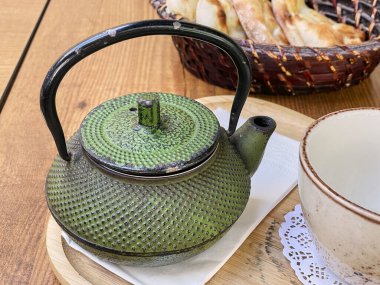 Geleneksel bir Japon dökme demir çaydanlığıyla, kırsal beyaz bir fincanla rahatlatıcı bir çay deneyiminin özünü yakala. Set, ahşap bir tepside zarif bir şekilde duruyor. Huzur ve sıcaklığı çağrıştırıyor..