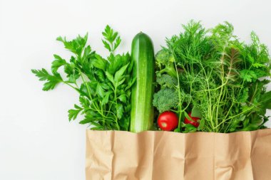 Beyaz arka planda, çevre dostu bir kese kağıdında taze sebze ve otların üst görüntüsü. Market alışverişi ve yemek teslimatı konsepti. Al!.