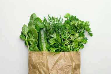 Beyaz arka planda, çevre dostu bir kese kağıdında taze sebze ve otların üst görüntüsü. Market alışverişi ve yemek teslimatı konsepti. Al!.