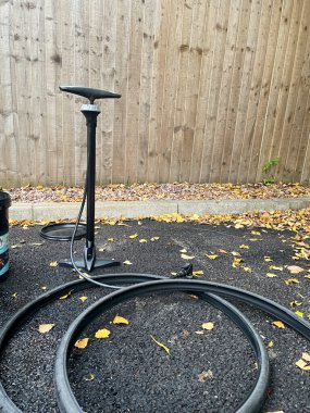 Bir bisiklet lastiği pompası ve asfaltta düşen sonbahar yapraklarıyla çevrili iç borular. Sahne ahşap bir çitin karşısına kurulmuş, açık hava bakımını yakalıyor..