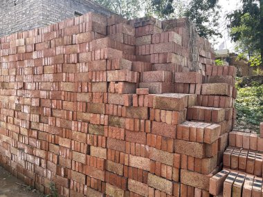 Bir inşaat sahasında düzgünce düzenlenmiş kırmızı ve kahverengi tuğla yığınları, inşaat projeleri ve inşaat çalışmaları için hazır hammaddeleri sergiliyor.