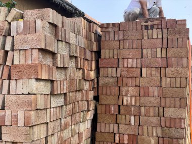 Eller bir yığın tuğlayı hortumla sularken görülüyor. İnşaat veya duvarcılık amaçlı olabilir. Görüntü, el emeği, inşaat ve sanayi kavramlarını iletir.