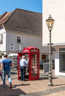 HOFHEIM AM TAUNUS, ALMANY-MAYIS 19, 2025: Eski kırmızı bir telefon kulübesinde ücretsiz bir sokak kütüphanesi