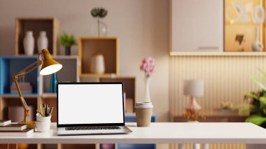 Ahşap masadaki beyaz ekranlı bir dizüstü bilgisayarın maketi, rahat bir oturma odasında dekoratif eşyalar eşliğinde...