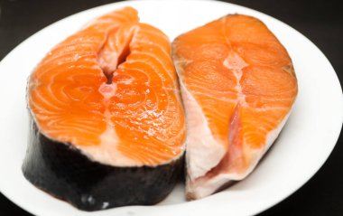 Siyah arka planda beyaz tabakta iki sulu somon bifteği.