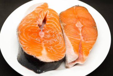 Siyah arka planda beyaz tabakta iki sulu somon bifteği.