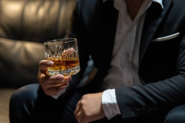 İş adamı içki deposunda elinde viski bardağıyla oturuyor.