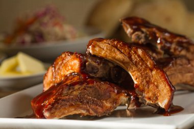 Tabakta ızgara BBQ kaburga eti, taze ve sağlıklı beslenme. Lahana salatası, taze ekmek ruloları, koçanda mısır, beyaz tabakta tuzlu tereyağı ve maşa ve eski ahşap masa içeren mezeler.