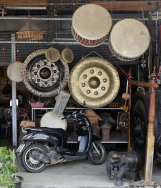 Sergilenen davul ve gonglar, fil heykeli ve diğer eşyalar gibi geleneksel Asya kültürel materyallerinin sergilendiği bir Tayland mağazasının dikey fotoğrafı..