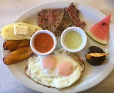 Taze malzemeler ve dengeli bir yemekle besleyici bir kahvaltı manzarası. Güneşli tarafı yukarı yumurta, tatlandırılmış muz. plantains, dips, et, tatlı ve karpuz