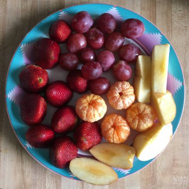 Olgun bir çileğin, üzümlerin, portakalların ve elmaların üzerinde mavi bir tabağın üzerinde.