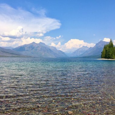 Buzul Ulusal Parkı, Montana 'daki McDonald Gölü' nde sakin su ve bulutlarla dolu sakin bir kıyı manzarası. 