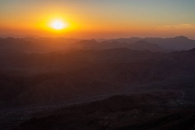 Huzurlu bir dağ gündoğumunun yatay fotoğrafı, dağların üzerinde sisli turuncu bir gökyüzü. Sina Yarımadası 'ndan gün doğumu. Sina Mısır