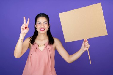 Genç bir kadın elinde bir bayrak tutuyor barış ve aşk sembolü yapıyor.