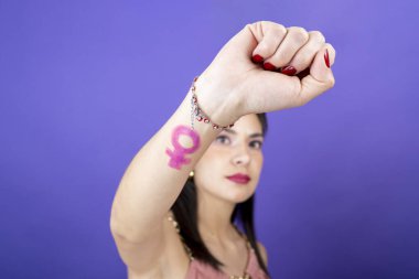 Kadının yumruğuna yakın çekim. İzole edilmiş menekşe kadife arka planda feminist sembolle yakın çekim.