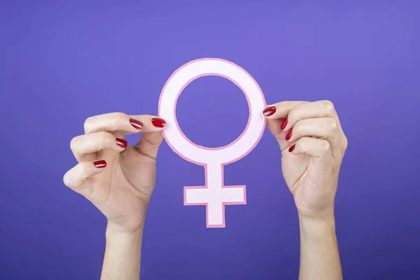 woman hands holding feminist symbol close up on purple velvet isolated background