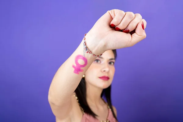 closeup of woman\'s fist close up with the feminist symbol on an isolated violet velvet background