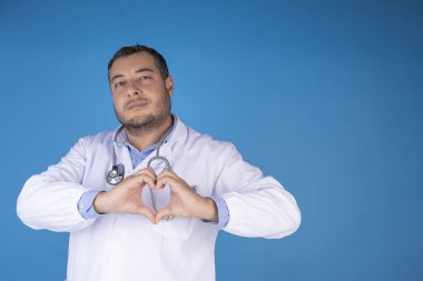 Doktor elleriyle izole edilmiş mavi bir arka planda kalp yapıyor.