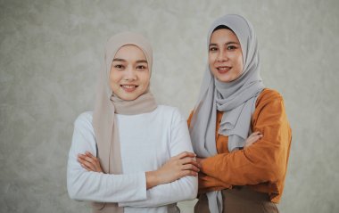 Resmi elbiseler ve türban takan iki İslamcı kadın kollarını kavuşturup kameraya bakarak güven ve dostça gülümsüyor..