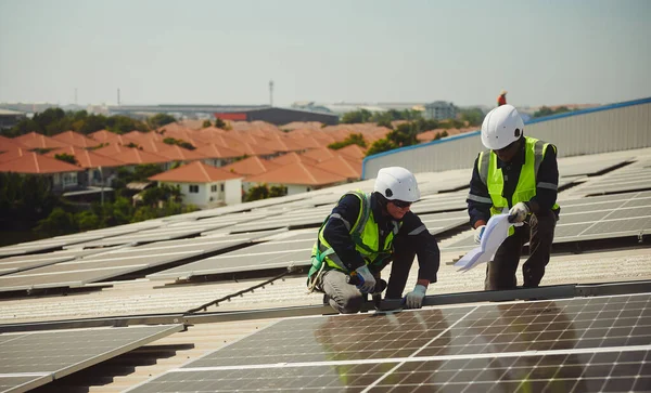 Two men of different nationalities wearing protective clothing for working on high-rise buildings install solar panels on the roof of a building.