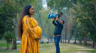 Kocası ve çocuğuyla birlikte genç hamile bir kadın, dışarıda eğleniyor, Hint aile kavramı.
