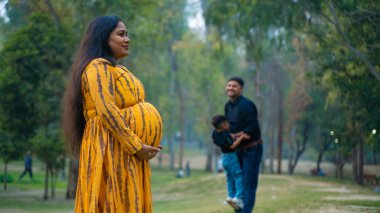 Kocası ve çocuğuyla birlikte genç hamile bir kadın, dışarıda eğleniyor, Hint aile kavramı.