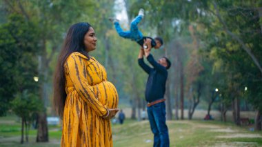 Kocası ve çocuğuyla birlikte genç hamile bir kadın, dışarıda eğleniyor, Hint aile kavramı.