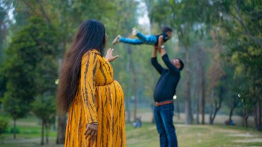 Kocası ve çocuğuyla birlikte genç hamile bir kadın, dışarıda eğleniyor, Hint aile kavramı.