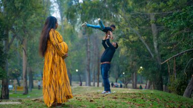 Kocası ve çocuğuyla birlikte genç hamile bir kadın, dışarıda eğleniyor, Hint aile kavramı.