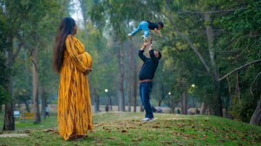 Kocası ve çocuğuyla birlikte genç hamile bir kadın, dışarıda eğleniyor, Hint aile kavramı.