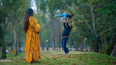 Kocası ve çocuğuyla birlikte genç hamile bir kadın, dışarıda eğleniyor, Hint aile kavramı.