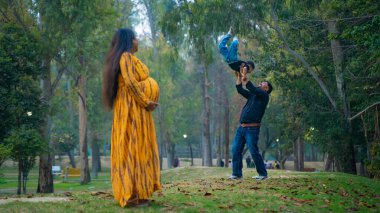 Kocası ve çocuğuyla birlikte genç hamile bir kadın, dışarıda eğleniyor, Hint aile kavramı.