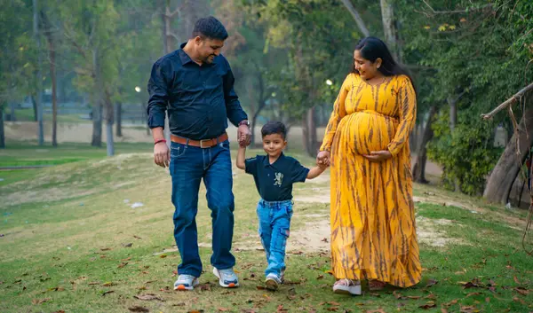 Kocası ve çocuğuyla birlikte genç hamile bir kadın, dışarıda eğleniyor, Hint aile kavramı.