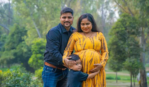 Kocası ve çocuğuyla birlikte genç hamile bir kadın, dışarıda eğleniyor, Hint aile kavramı.