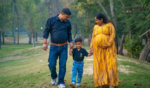 Kocası ve çocuğuyla birlikte genç hamile bir kadın, dışarıda eğleniyor, Hint aile kavramı.