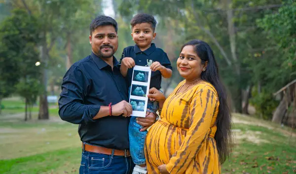 Kocası ve çocuğuyla birlikte genç hamile bir kadın, dışarıda eğleniyor, Hint aile kavramı.