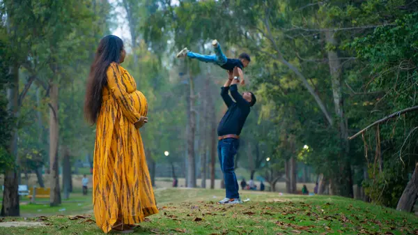 Kocası ve çocuğuyla birlikte genç hamile bir kadın, dışarıda eğleniyor, Hint aile kavramı.