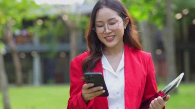 Asyalı iş kadını cep telefonu kullanıyor, akıllı telefonuyla modern ofis dışındaki iş arkadaşlarıyla mesajlaşıyor ve sohbet ediyor..