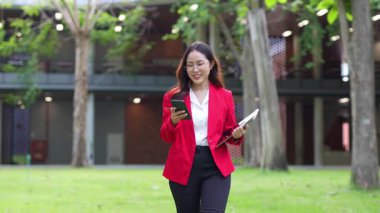 Asyalı iş kadını cep telefonu kullanıyor, akıllı telefonuyla modern ofis dışındaki iş arkadaşlarıyla mesajlaşıyor ve sohbet ediyor..